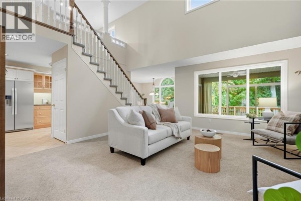 Living room with a cream sofa, two wooden side tables, and a large window. - 784 Gordon Street Unit# 20, Guelph