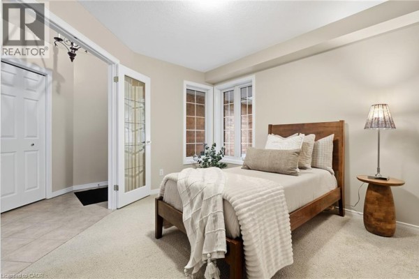 Bedroom with a wooden bed frame, beige carpet, and double-hung windows. - 784 Gordon Street Unit# 20, Guelph