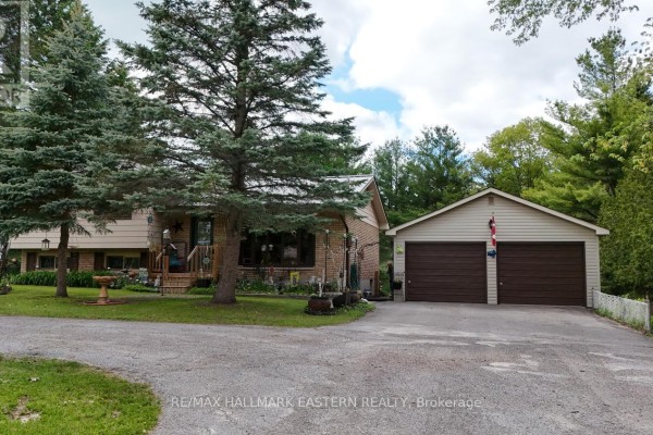 View of a house with a detached two-car garage and a gravel driveway bordered by trees and grass. - 784 Old Norwood Road, Havelock Belmont Methuen