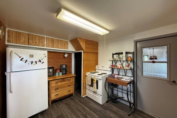 Kitchen with white stove, wood-paneled cabinets, and dark wood-look flooring looking towards the door. - 785 Bond Street, Cartwright
