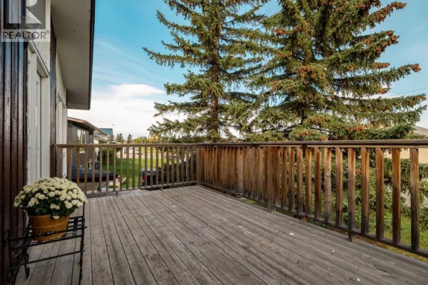 Wooden deck with railing and a potted plant, overlooking the backyard. - 786 Isabel, Pincher Creek