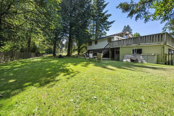 Side view of the house showing a large grassy yard, mature trees, and a wooden fence. - 7876 139a Street, Surrey