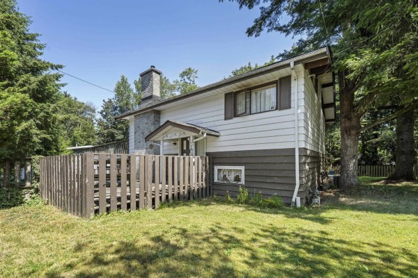 Exterior of the house with white siding, dark brown trim, a stone chimney, and a wooden deck. - 7876 139a Street, Surrey