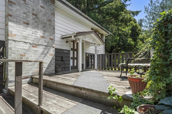 Wooden deck with stairs and a walkway leading to the front entrance of the house. - 7876 139a Street, Surrey