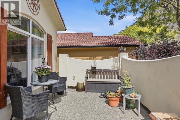 A patio area with two chairs, a small table, and a bench, surrounded by a stucco wall. - 788 Rosewood Crescent, Kamloops