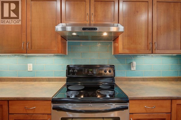 Close-up of a stainless steel stove and hood fan with turquoise subway tile backsplash. - 788 Rutland Road N Unit# 6, Kelowna