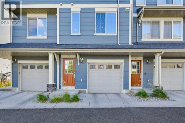 Close-up view of the exterior of a blue townhouse with garages and front doors at units 79 and 75. - 79 Evansview Gardens Nw, Calgary