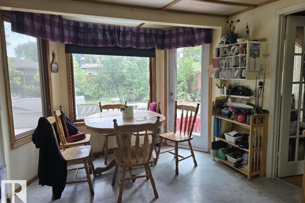 Breakfast nook with a round wooden table and chairs, a large window, and a door leading to the backyard. - 79 Gariepy Cr Nw, Edmonton
