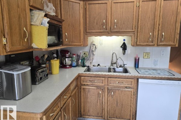 Kitchen with oak cabinets, a double sink, a white dishwasher, microwave, and a toaster on the counter. - 79 Gariepy Cr Nw, Edmonton
