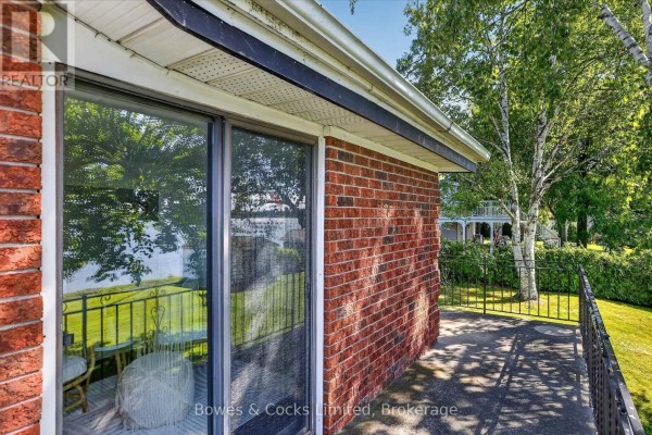 Side view of the house showing a sloped lawn, multi-level decks, and surrounding trees. - 79 Oakdene Crescent, Kawartha Lakes