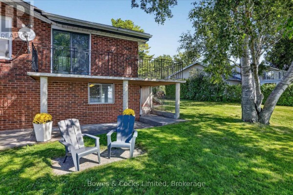 Close-up of the house exterior featuring a sunroom with a lake view and chairs on the patio. - 79 Oakdene Crescent, Kawartha Lakes