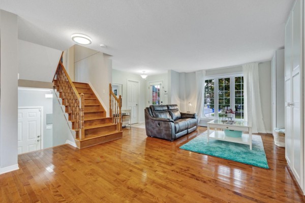 Living room with hardwood floors, a dark leather sofa, and a white coffee table on a teal rug. - 79 Rue Du Frimas, Gatineau