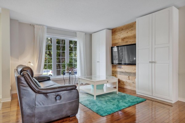 Living room showing a leather sofa, white cabinets, and a TV mounted on a wood-paneled wall. - 79 Rue Du Frimas, Gatineau