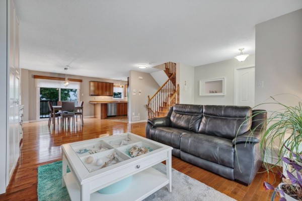 Living area with sofa and coffee table, opening to a dining area and kitchen with wooden cabinets. - 79 Rue Du Frimas, Gatineau