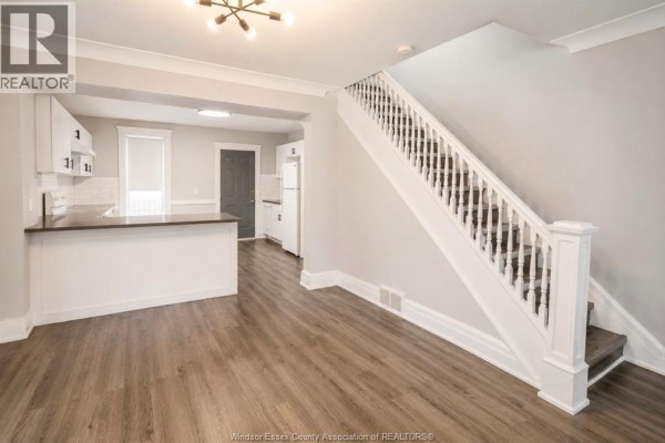 Open-concept living area with white kitchen, stairs, and wood-look flooring. - 790 Marentette, Windsor