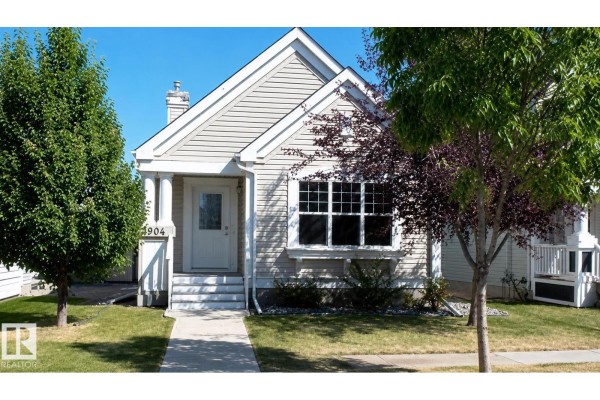 Living room with grey sectional sofa, wood floors, vaulted ceiling, and dining area view. - 7904 13 Av Sw, Edmonton