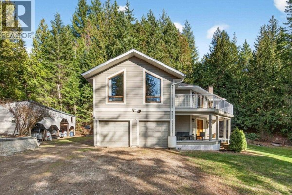 Grey house with two garage doors and a covered porch under a daytime sky, surrounded by trees. - 7905 97a Highway, Mara