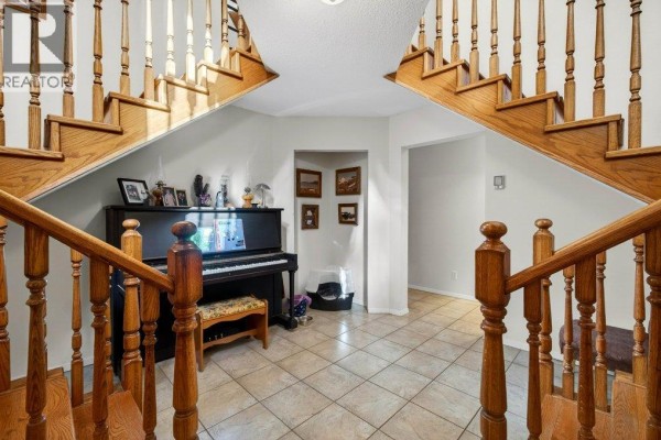 Interior hallway with a black upright piano, tiled floor, and a split staircase with wooden railings. - 7905 97a Highway, Mara