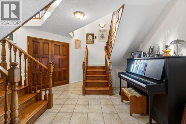 Interior hallway with a black upright piano, double wooden doors, and a split staircase with wooden railings. - 7905 97a Highway, Mara