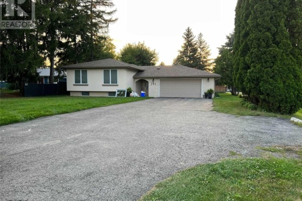 A cream-colored bungalow with a double garage and driveway, surrounded by green lawn and mature trees. - 791 Essa Road, Barrie
