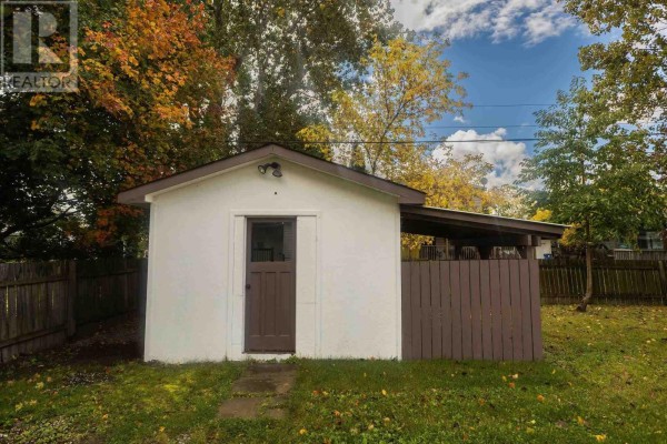 White shed with a brown door and a covered lean-to in a grassy backyard. - 791 Second Lin W, Sault Ste  Marie