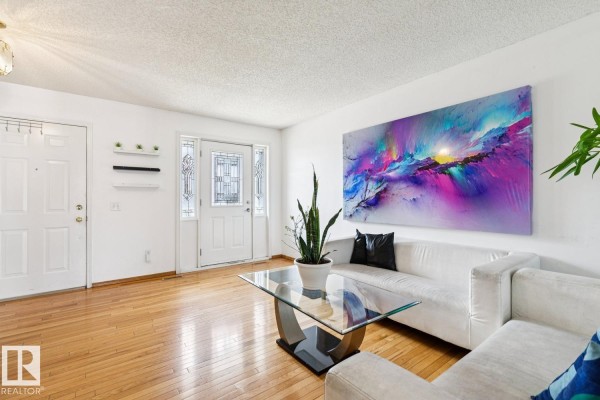 Living room with white couches, a glass coffee table, hardwood floors, and a large abstract painting. - 7912 154 Av Nw, Edmonton