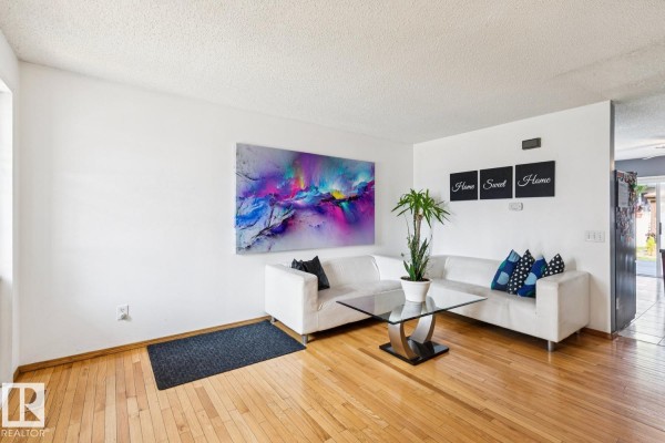 Living room with white sectional sofa, glass coffee table, hardwood floors, and wall decor. - 7912 154 Av Nw, Edmonton