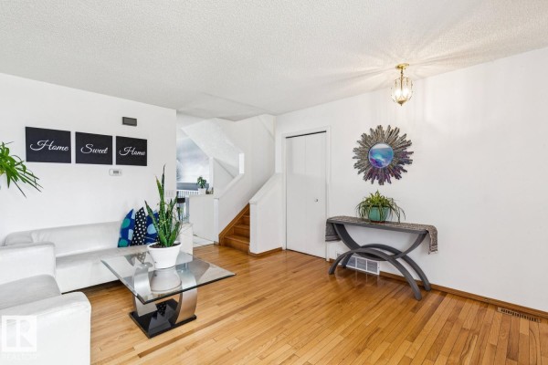 Living room with a sofa, glass coffee table, hardwood floors, and a staircase leading upstairs. - 7912 154 Av Nw, Edmonton