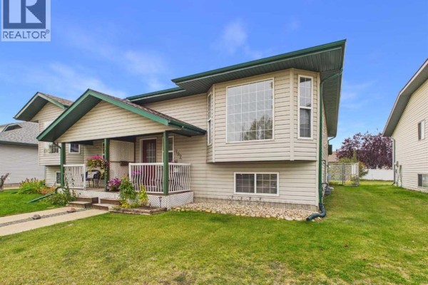 Side exterior view of a beige duplex with large bay windows on the upper level and smaller windows below. - 792 Lancaster Drive, Red Deer