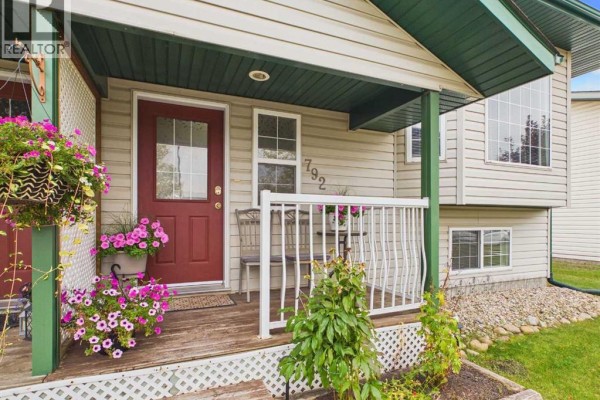 Detail of a red front door on a duplex porch with a white railing, bench, and potted flowers. - 792 Lancaster Drive, Red Deer