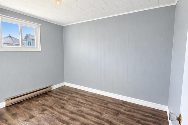 Empty room with light blue paneled walls, wood-look laminate flooring, and a small window. - 792 Random Island Road, Elliott S Cove