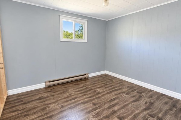 Empty room with light blue paneled walls, wood-look laminate flooring, and a small window. - 792 Random Island Road, Elliott S Cove