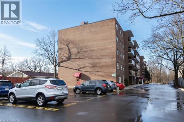 Side view of brick apartment building with parked cars and clear sky - 793 Colborne Street Unit# 205, Brantford