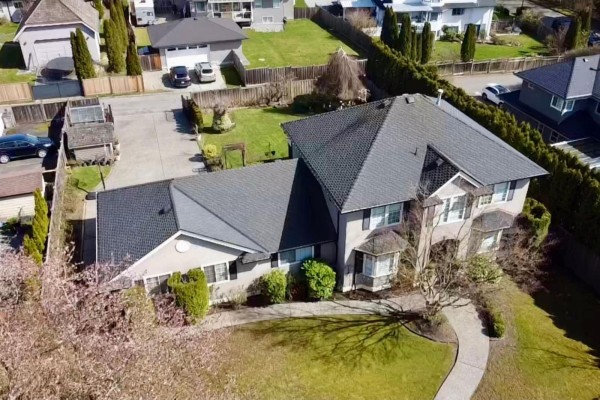 Exterior of a tan stucco home with a manicured lawn and trees. - 7930 144 Street, Surrey