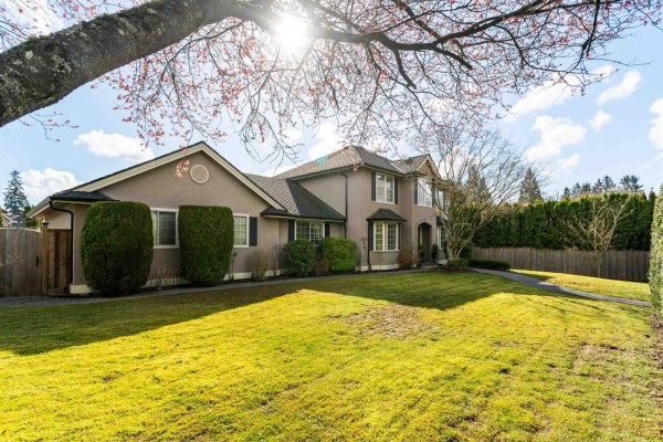 Side exterior view of a tan stucco house with bay windows and manicured landscaping. - 7930 144 Street, Surrey