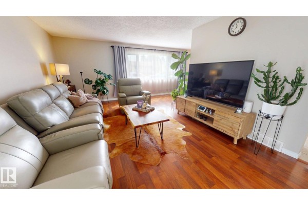 Living room with light grey sofas, a live edge coffee table, and a large television. - 7935 22 Av Nw, Edmonton