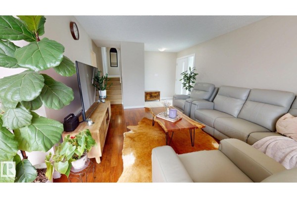 Living room with large grey sectional sofa, wooden media console, and stairs to upper level. - 7935 22 Av Nw, Edmonton