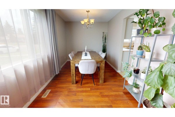 Dining room with a wooden table and chairs, set by a large window with sheer curtains. - 7935 22 Av Nw, Edmonton