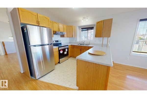Kitchen with light wood cabinets, stainless steel refrigerator, black stovetop, and white countertop. - 7936 3 Av Sw, Edmonton