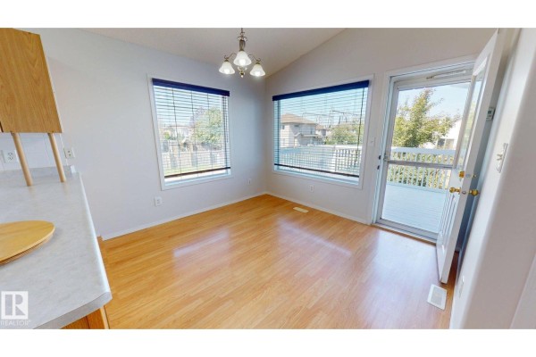 Dining area with light wood laminate flooring, white walls, and windows overlooking a backyard. - 7936 3 Av Sw, Edmonton
