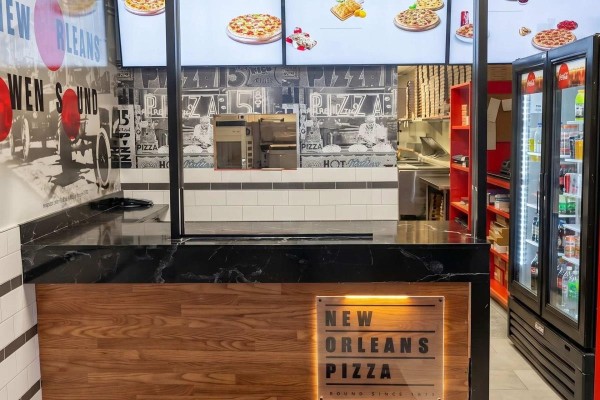 Counter area of a pizza restaurant with black marble top, wood paneling, and beverage coolers. - 795 9th Avenue E, Owen Sound