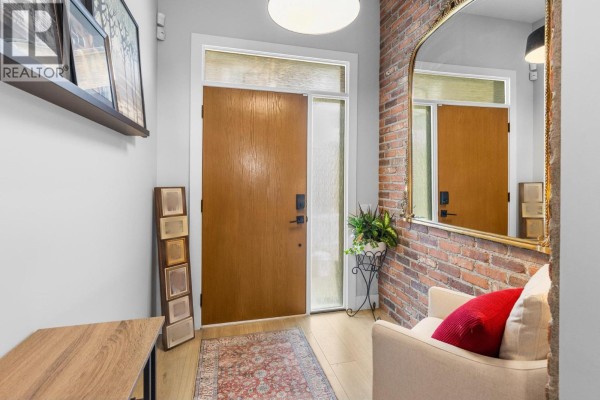Interior foyer with wood door, brick wall accent, mirror, and light wood flooring. - 796 Kuipers Crescent Unit# 2, Kelowna