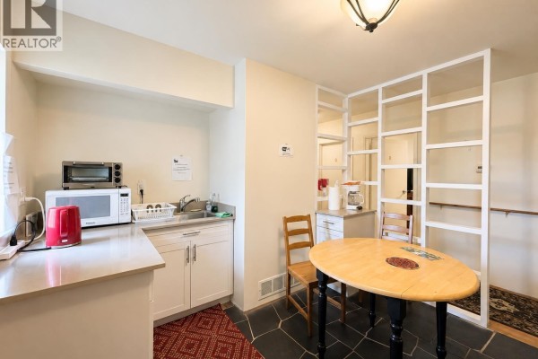 Small kitchen area with light wood cabinets, dark stone floor, and an oval dining table. - 796 W 42nd Avenue, Vancouver