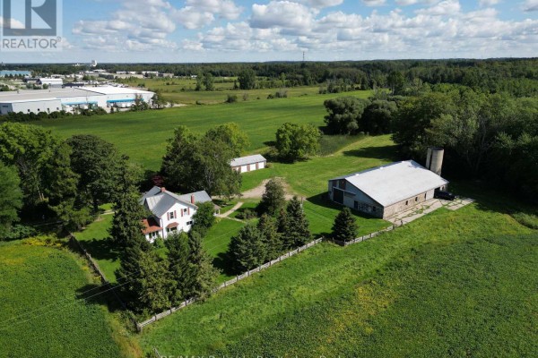 Wide aerial view of a farm property with surrounding agricultural fields and industrial buildings in the distance. - 79888 Bluewater Highway, Central Huron