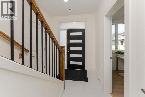 Bright white entryway with a black front door featuring horizontal glass panels and a wooden staircase. - 7990 Southridge Avenue, Prince George