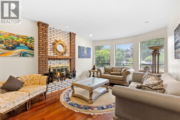 Living room with a brick fireplace, large windows, and upholstered seating. - 7995 Woodhurst Drive, Burnaby