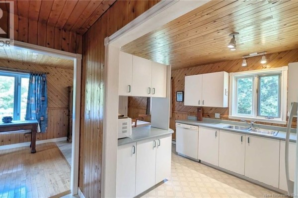 White kitchen cabinets and countertops in a room with wood-paneled walls and linoleum flooring. - 7997 Rue Saint-paul, Bas Caraquet