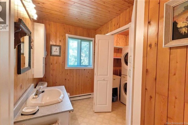 Bathroom with wood-paneled walls, a vanity, toilet, and stacked washer and dryer behind a closed door. - 7997 Rue Saint-paul, Bas Caraquet