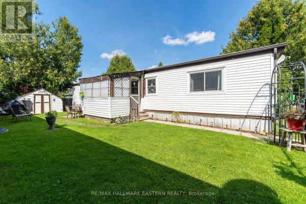 Rear exterior of the mobile home showing a grassy yard and storage shed. - 7a - 2244 Heritage Line, Otonabee South Monaghan