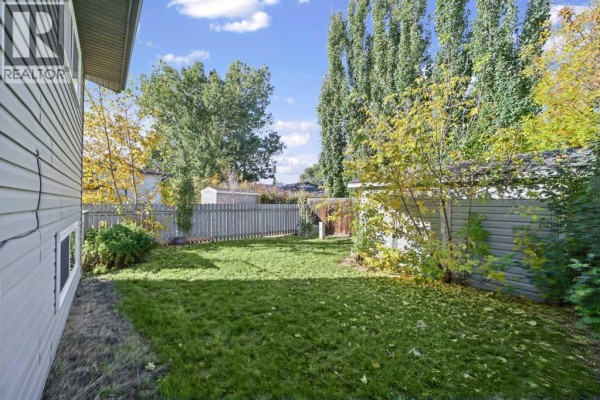 View of a fenced backyard with a green lawn, trees, and a shed. - 7a Westhill Place, Didsbury